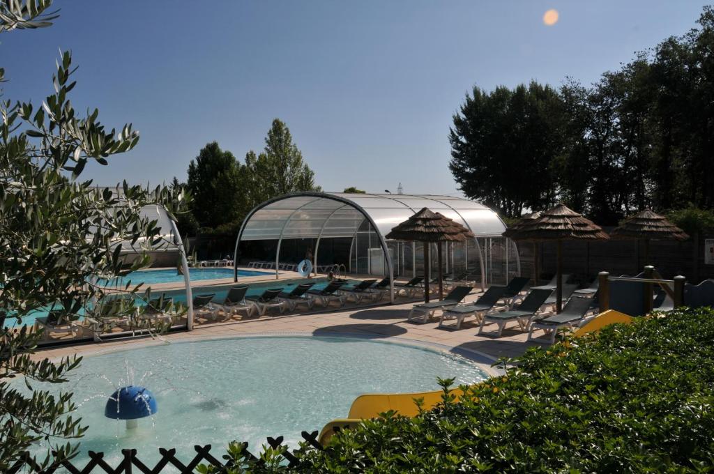 a swimming pool with chairs and umbrellas and a building at Camping La Mignardière in Ballan-Miré