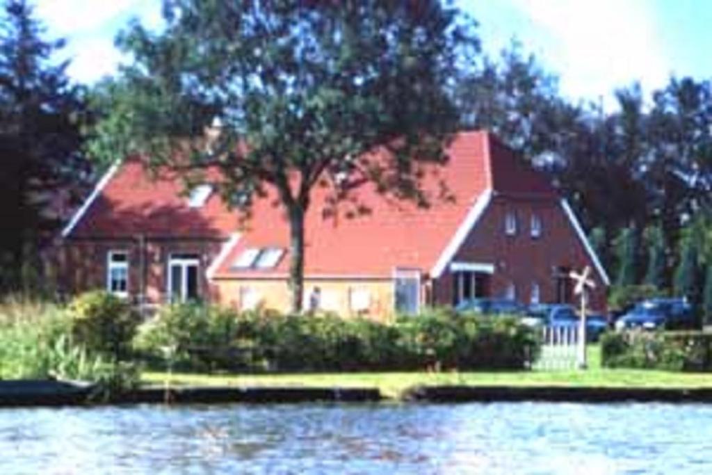 a large red house with a tree in front of a lake at Ferienwohnung am Sandwater 