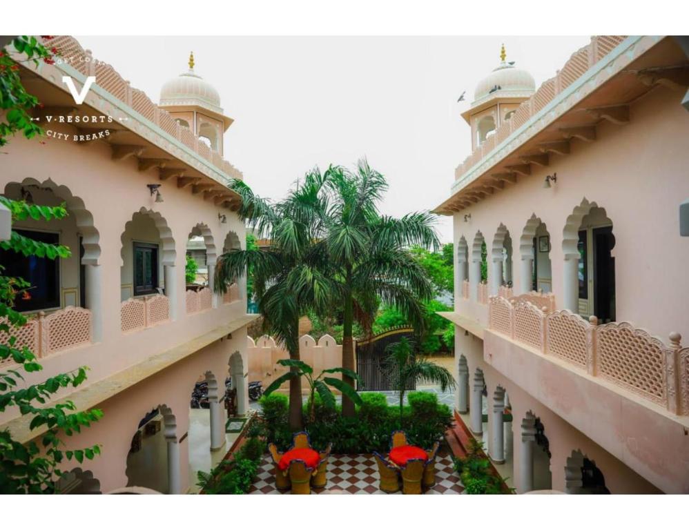 a building with a courtyard with palm trees and red umbrellas at Hotel Kiran Villa Palace, Bharatpur in Bharatpur