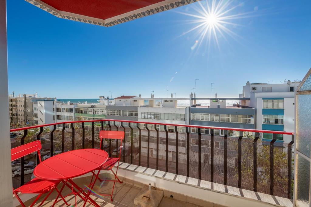 クアルテイラにあるVita Portucale ! Quarteira Sea Viewの赤い椅子付きのバルコニーから市街の景色を望めます。