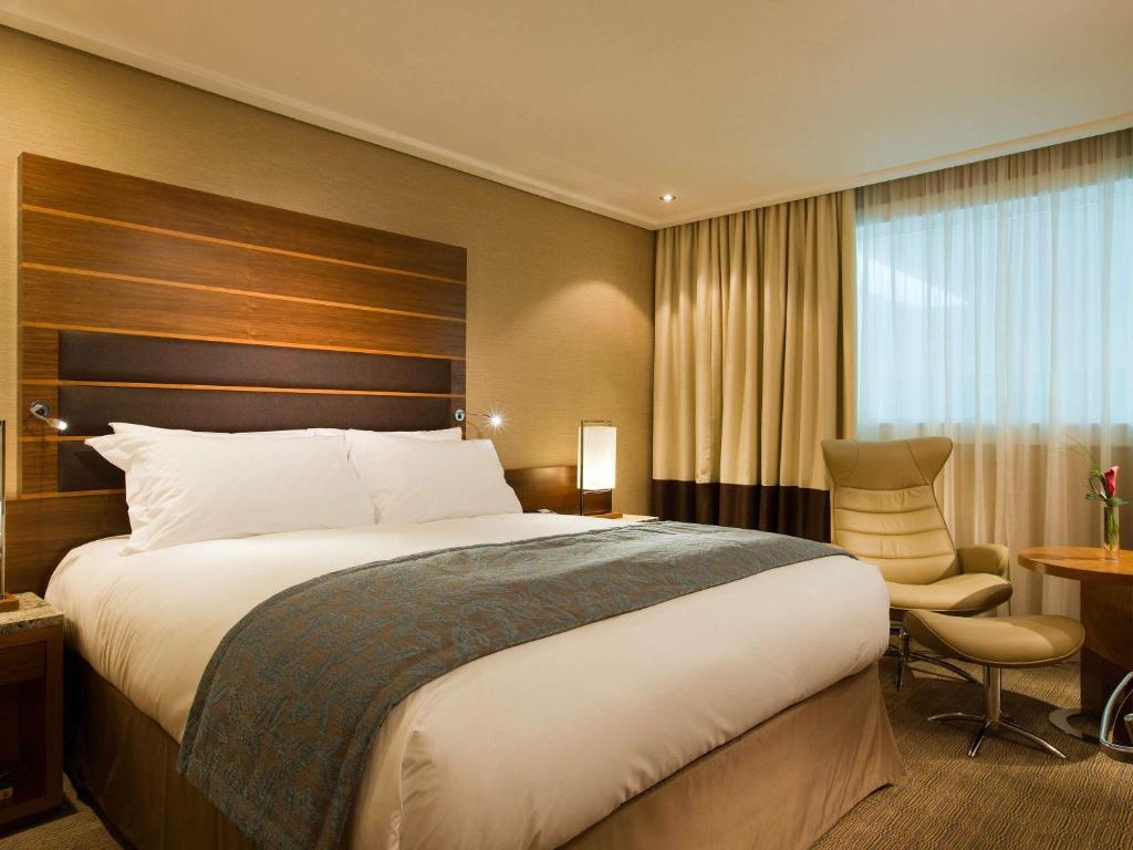 ヒリンドンにあるソフィテル ロンドン ヒースローの大きなベッドと椅子が備わるホテルルームです。