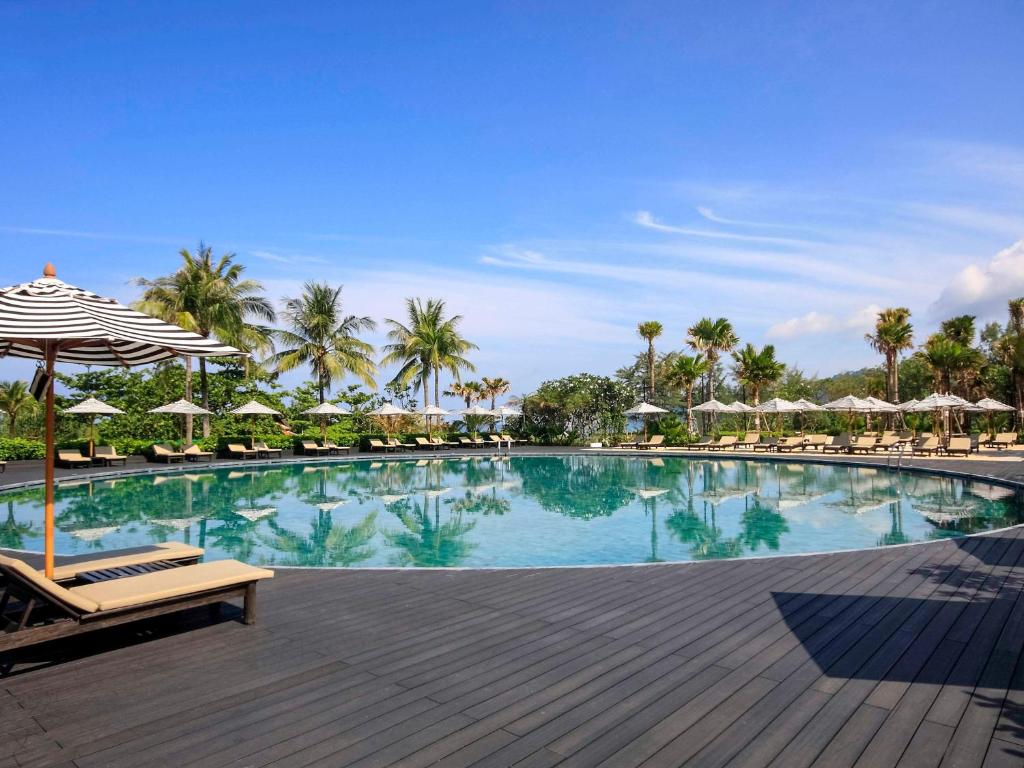 a pool with chairs and umbrellas on a wooden deck at Pullman Phuket Karon Beach Resort in Karon Beach