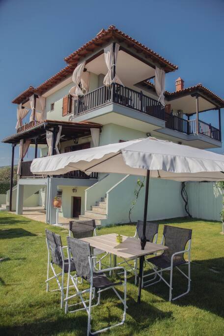 a table and chairs with an umbrella in front of a building at BS Village green in Metamorfosi