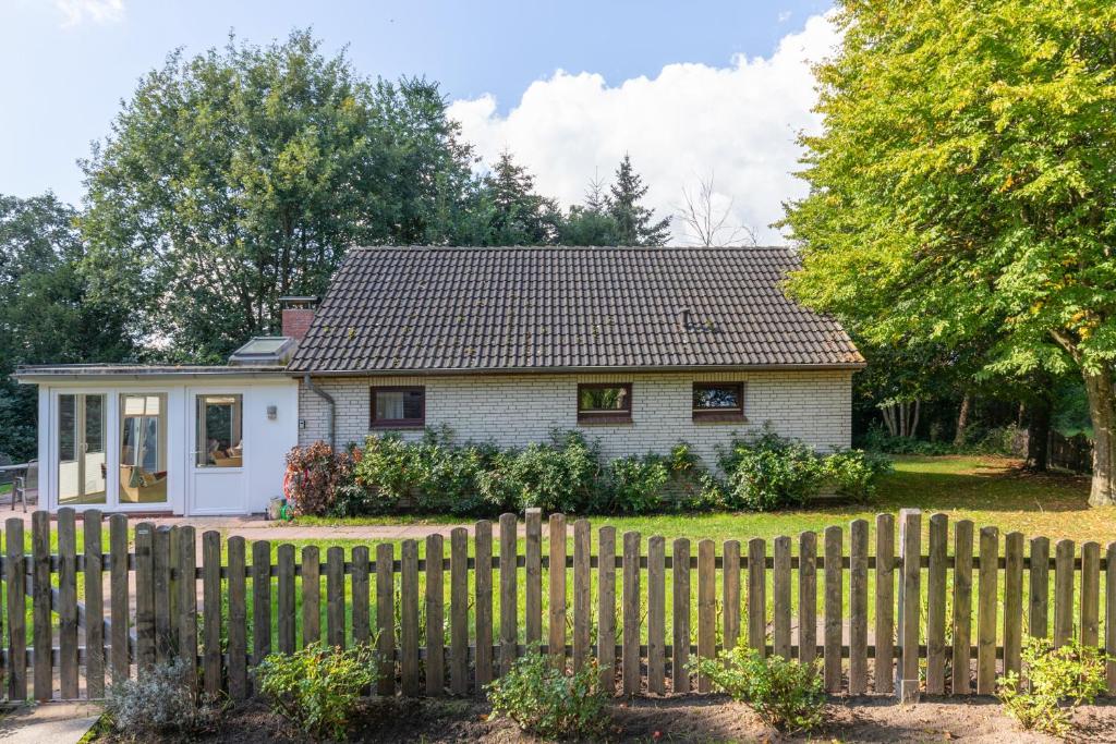 uma pequena casa branca atrás de uma cerca de madeira em Heidehaus em Enge-Sande