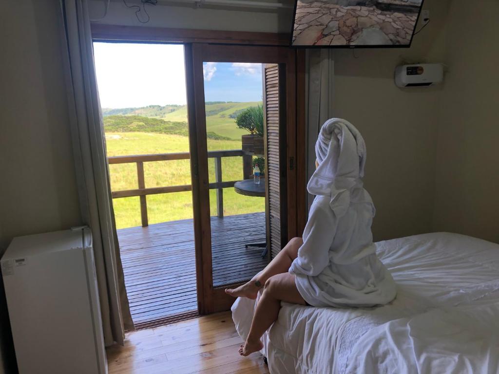 Eine Frau im Bademantel, die auf einem Bett sitzt und aus dem Fenster schaut. in der Unterkunft Vale de cambara II in Cambará