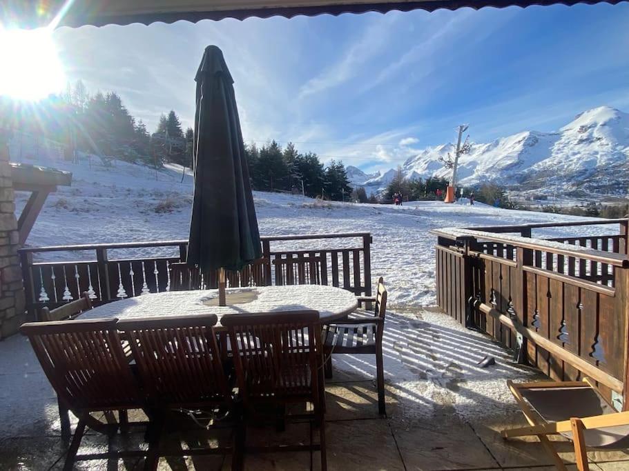 a table with an umbrella on a deck with snow covered mountains at Joue du Loup, appartement F3, pied des pistes in Le Dévoluy