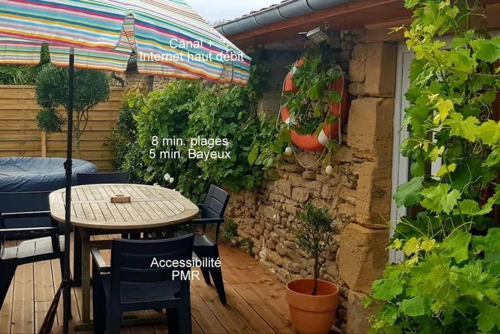 a patio with a table and chairs and a stone wall at L'Ancre du Bessin - Proximité Bayeux et plages du débarquement - D-DAY - Spa en option - Accessible PMR in Saint-Vigor-le-Grand