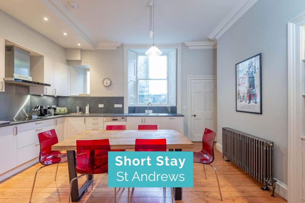 uma cozinha com uma mesa de madeira e cadeiras vermelhas em Luxury St Andrews Apartment - 5 mins to Old Course em St. Andrews