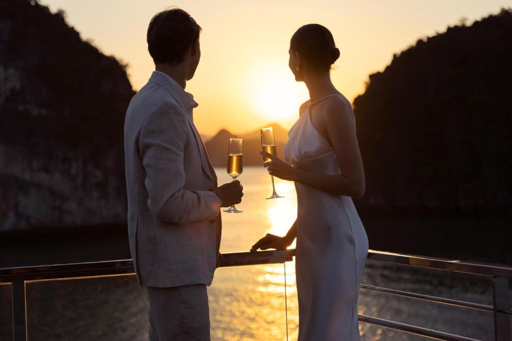 a man and a woman standing on a balcony with wine glasses at Grand Pioneers Halong Bay Cruise 1 in Ha Long