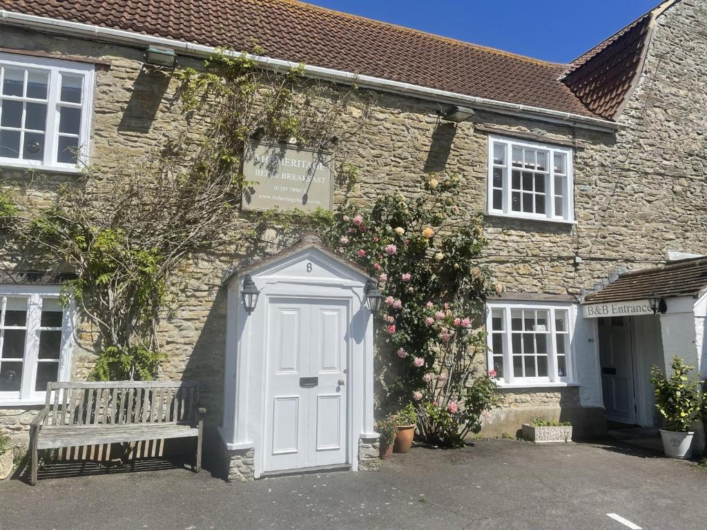 une maison en pierre avec une porte blanche et un banc dans l'établissement The Heritage Bed and Breakfast, à Weymouth