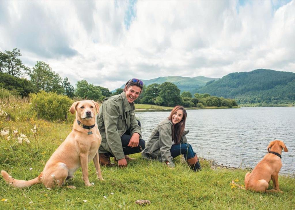 a man and a woman and two dogs sitting next to a lake at Bassenthwaite Lakeside Lodges in Bassenthwaite