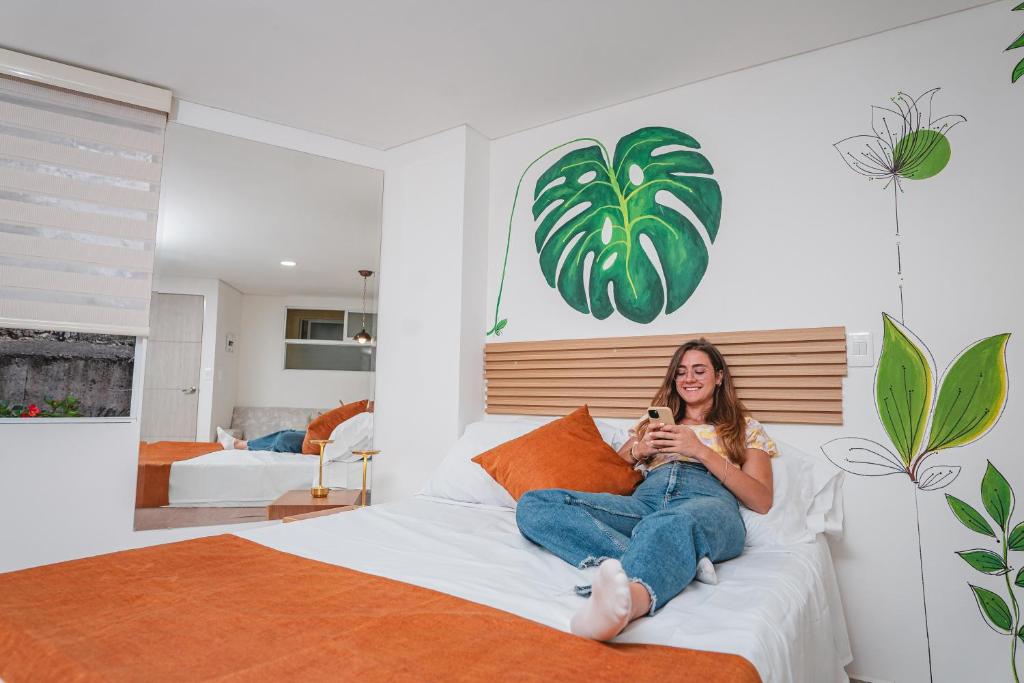 a woman sitting on a bed holding a cell phone at FLORA New & beautiful studio apartment with rooftop in Cali