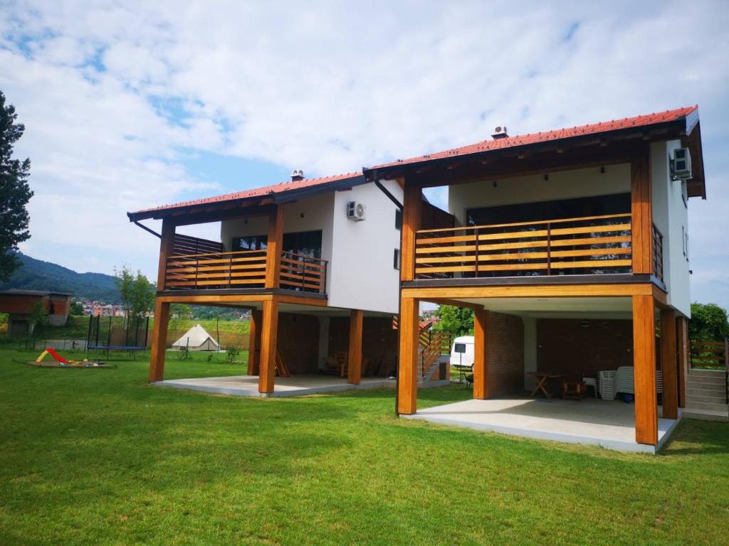 a house with a balcony and a grass yard at Banja na Drini - Lux vikendice na obali reke in Banja Koviljača