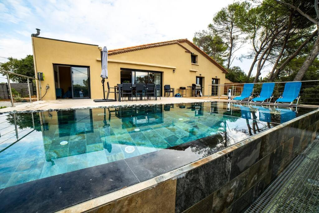 une piscine avec des chaises bleues et une maison dans l'établissement VILLA PISCINE MIROIR ET JACUZZI, à Saint-Bauzille-de-Montmel