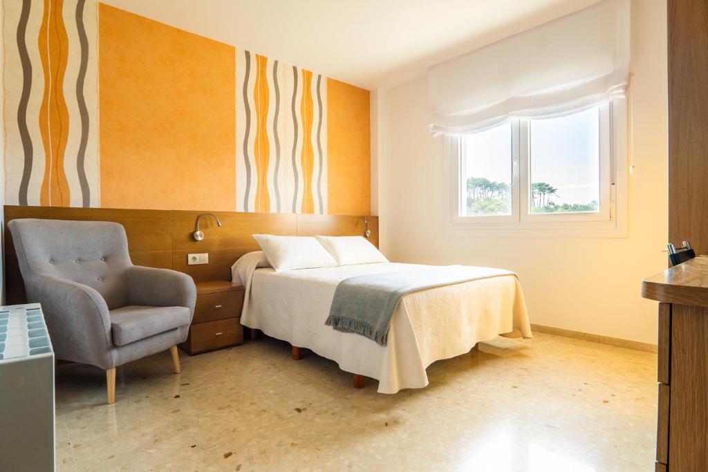 a bedroom with a bed and a chair and a window at Pensión Casa Alvarito in Portonovo