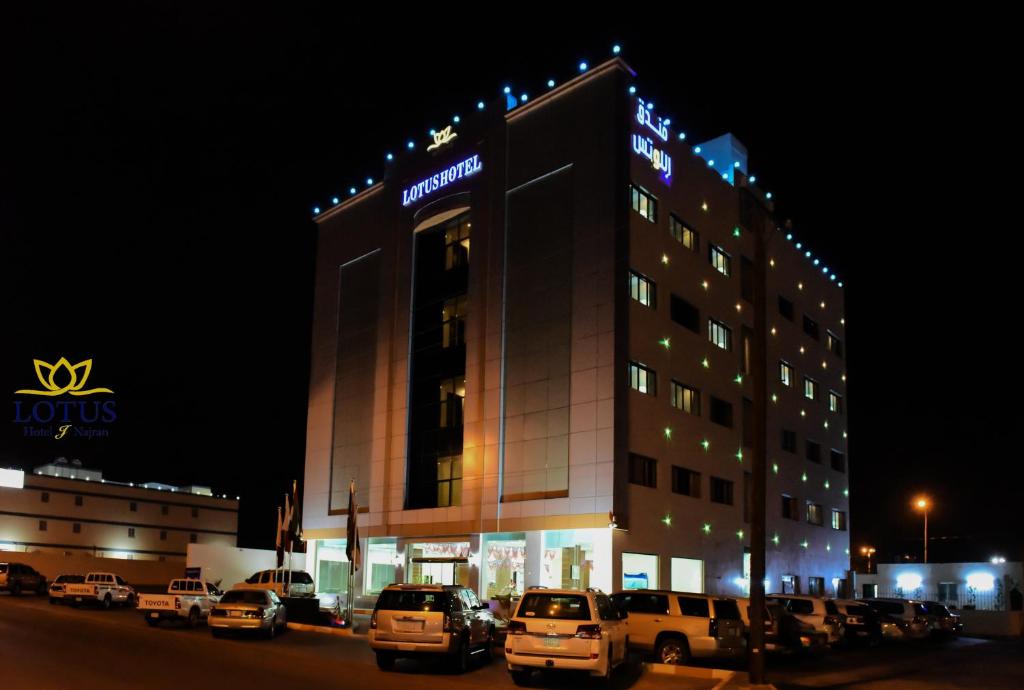 un bâtiment avec des voitures garées dans un parking la nuit dans l'établissement فندق اللوتس, à Najran