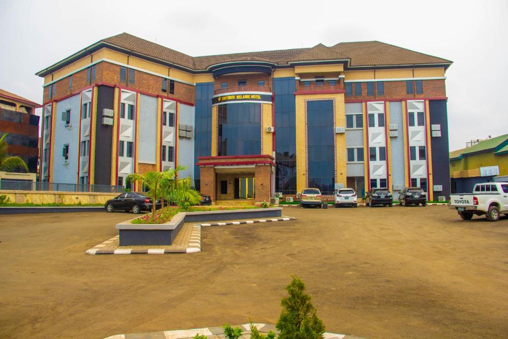 a large building with cars parked in a parking lot at Emperor Melanie Hotels in Awka