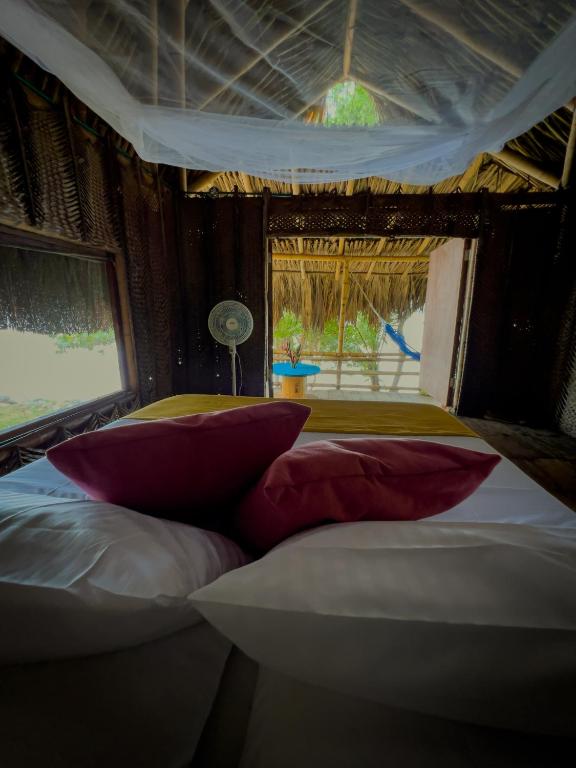 a room with a bed with pillows and a window at Los Achiotes Hostal - Palomino in Palomino