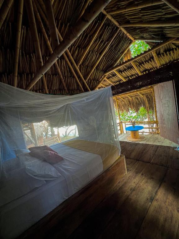 a bed in a straw hut with a mosquito net at Los Achiotes Hostal - Palomino in Palomino