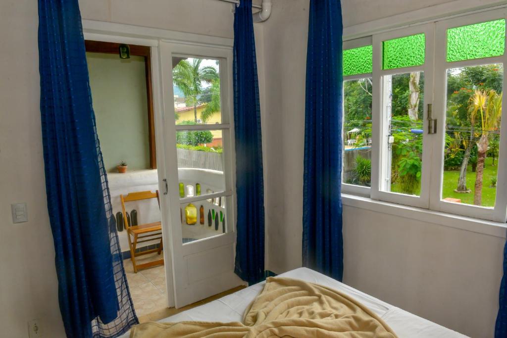 a bedroom with a bed with blue curtains and a window at Verde Vida Ecopousada - Termas do Gravatal in Gravatal