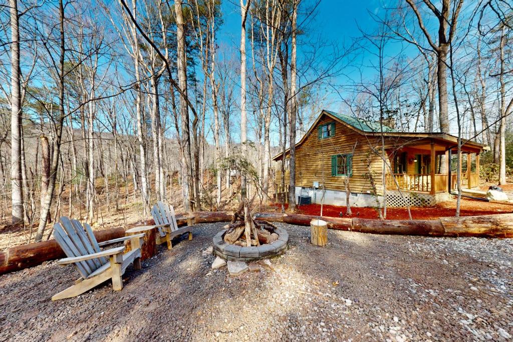 a log cabin in the woods with two chairs and a bench at Pine Tree Lodge in Sautee Nacoochee