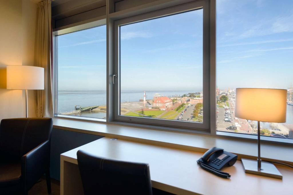 a desk with a lamp and a phone in front of a window at Atlantic Hotel Sail City in Bremerhaven