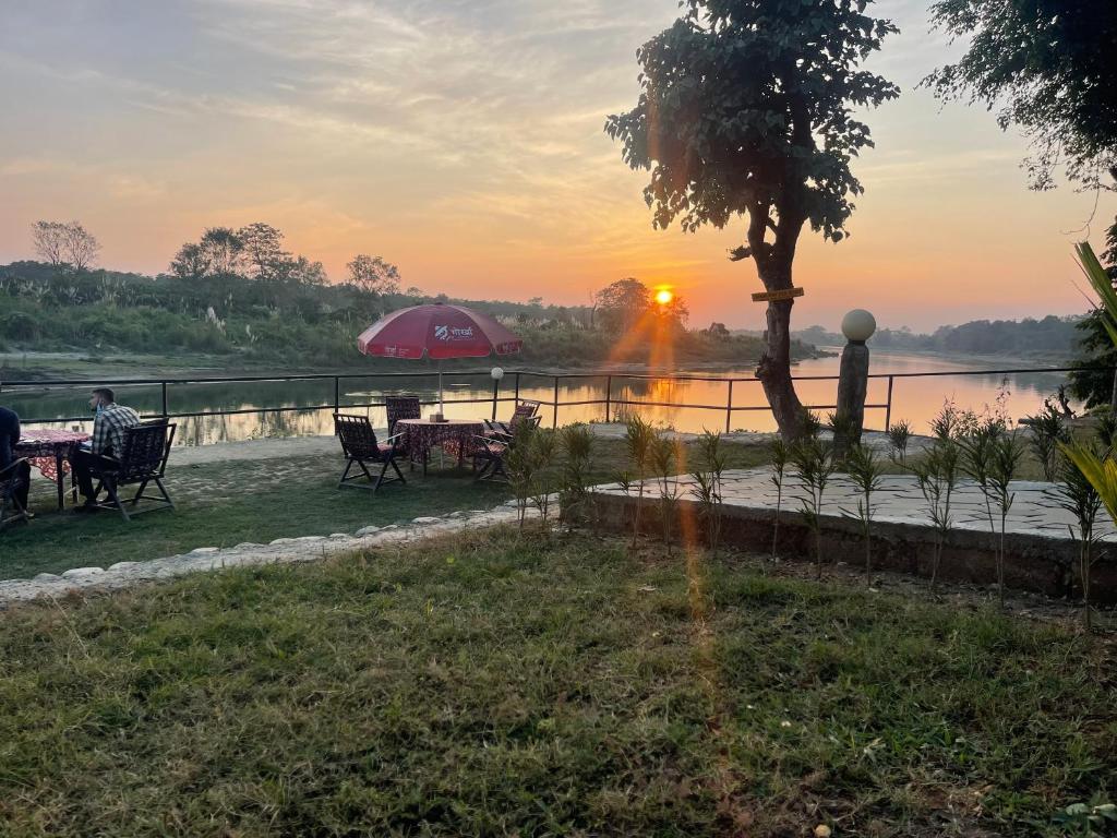 a sunset over a river with people sitting at tables at Chitwan Riverside Resort in Sauraha