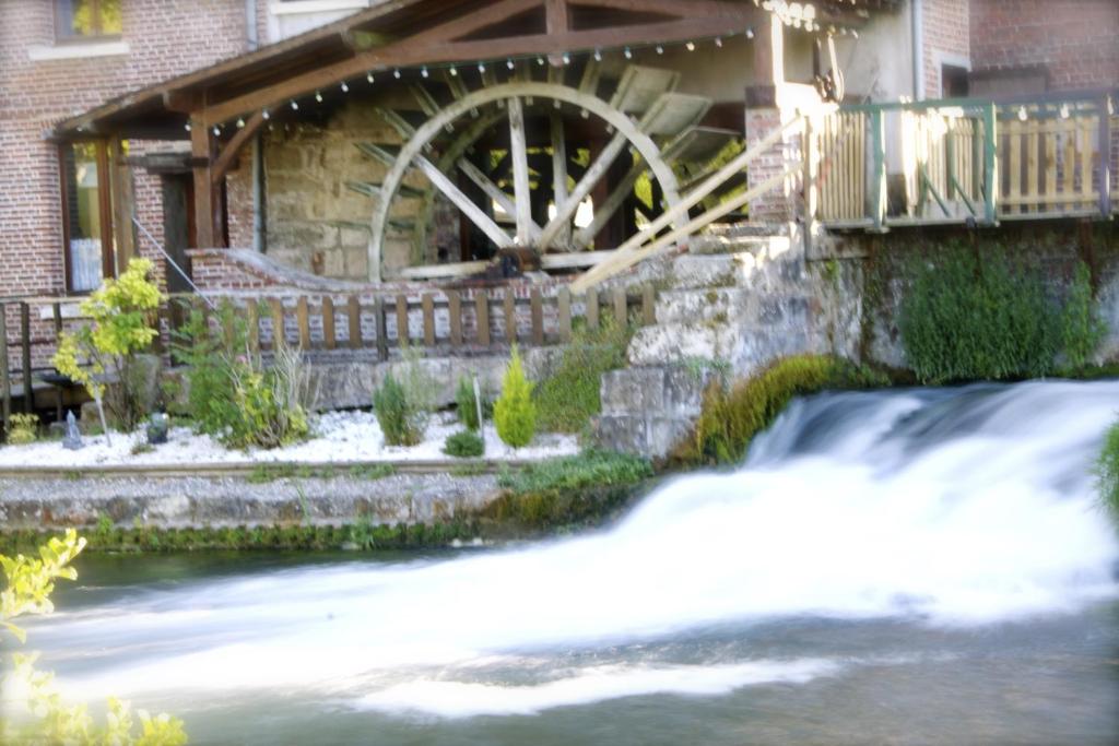 a waterwheel on the side of a house with a waterfall at Logis - Hôtel & Restaurant Moulin Des Forges in Saint-Omer-en-Chaussée