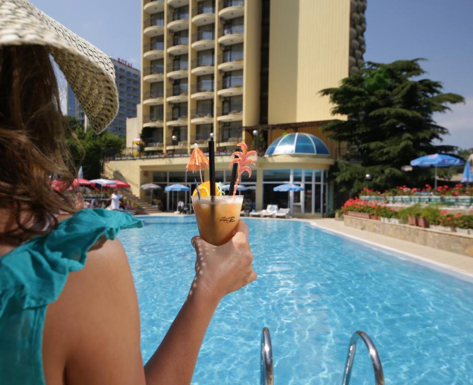 una mujer sosteniendo una bebida frente a una piscina en Hotel Shipka en Golden Sands