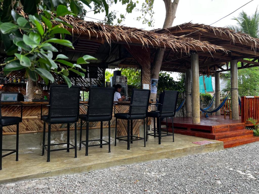 bar z czarnymi krzesłami siedzącymi pod dachem w obiekcie The Backyard Inn w mieście Moalboal