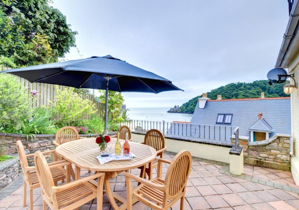 a wooden table with chairs and an umbrella at Riversea Cottage in Dartmouth