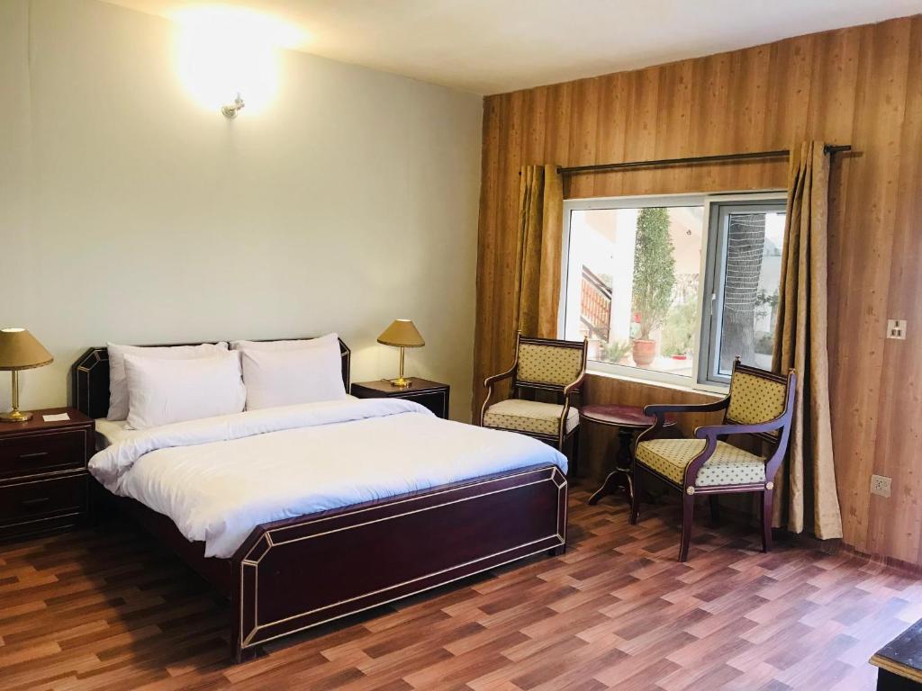 sypialnia z łóżkiem, 2 krzesłami i oknem w obiekcie The Sarai Suites, Murree w mieście Murree