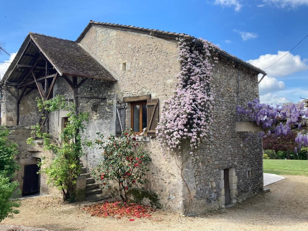 een oud stenen gebouw met paarse bloemen erop bij Gîte de charme La Pocterie in Vouneuil-sur-Vienne