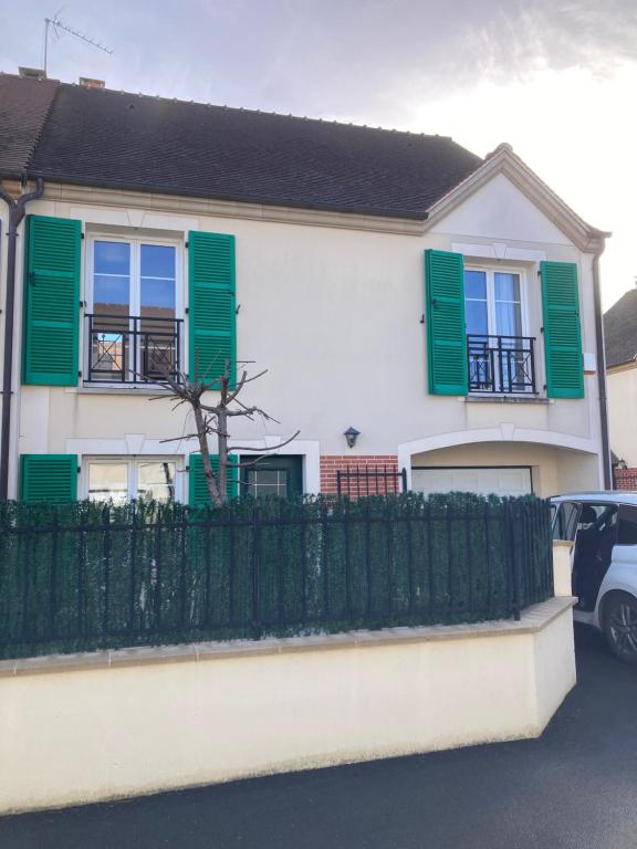 a white house with green shutters and a fence at La Maison des Massena in Noisy-le-Grand