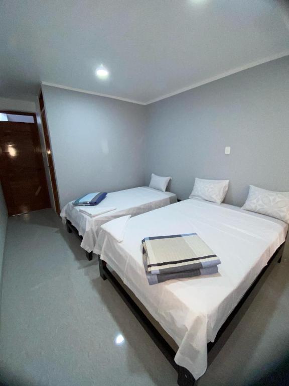 two beds in a room with white walls at Hostal Huella in Lambayeque