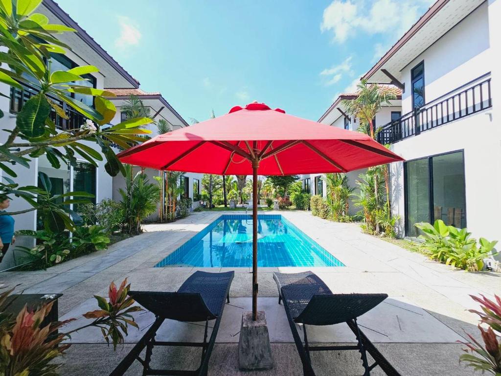 a red umbrella and chairs next to a swimming pool at KRAAM VILLAS in Thalang