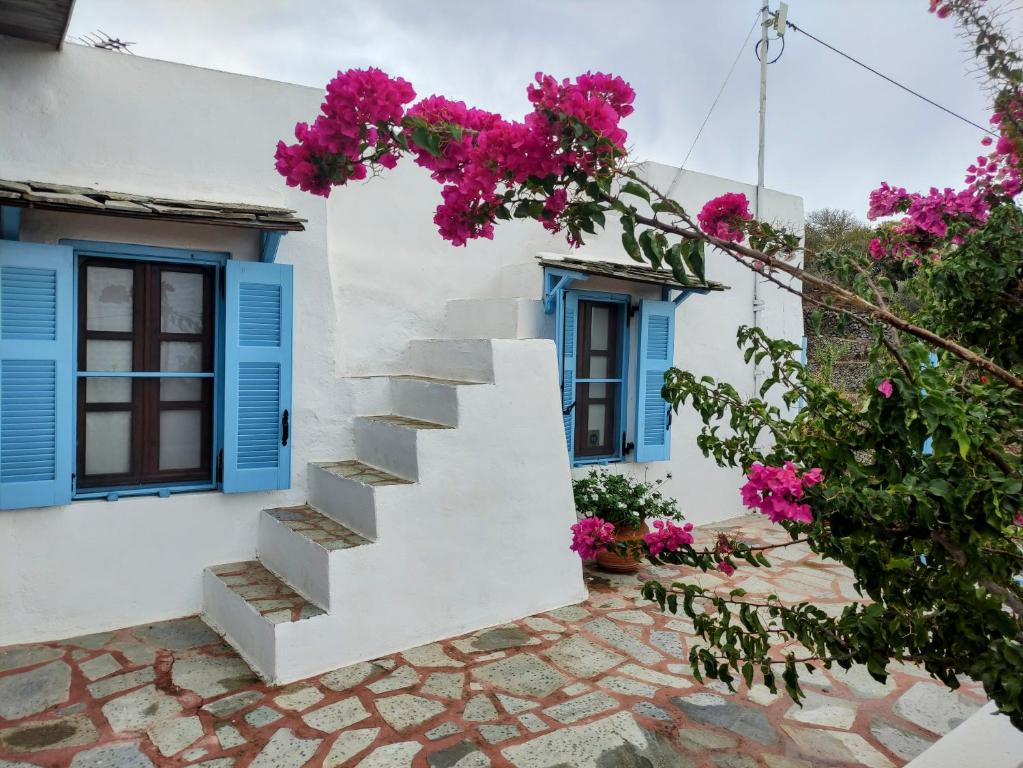 biały dom z niebieskimi oknami i różowymi kwiatami w obiekcie «Astrofeggia» A private stone house Nature-Seaview w mieście Mandrákion
