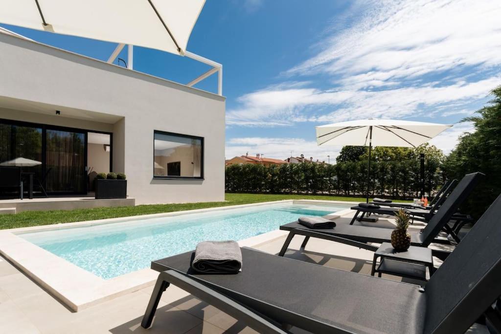 uma piscina com duas cadeiras e um guarda-sol em Villa Costa em Funtana