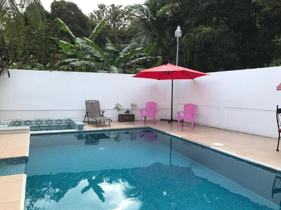 una piscina con sombrilla y sillas rojas en Casa del Árbol, en Quepos
