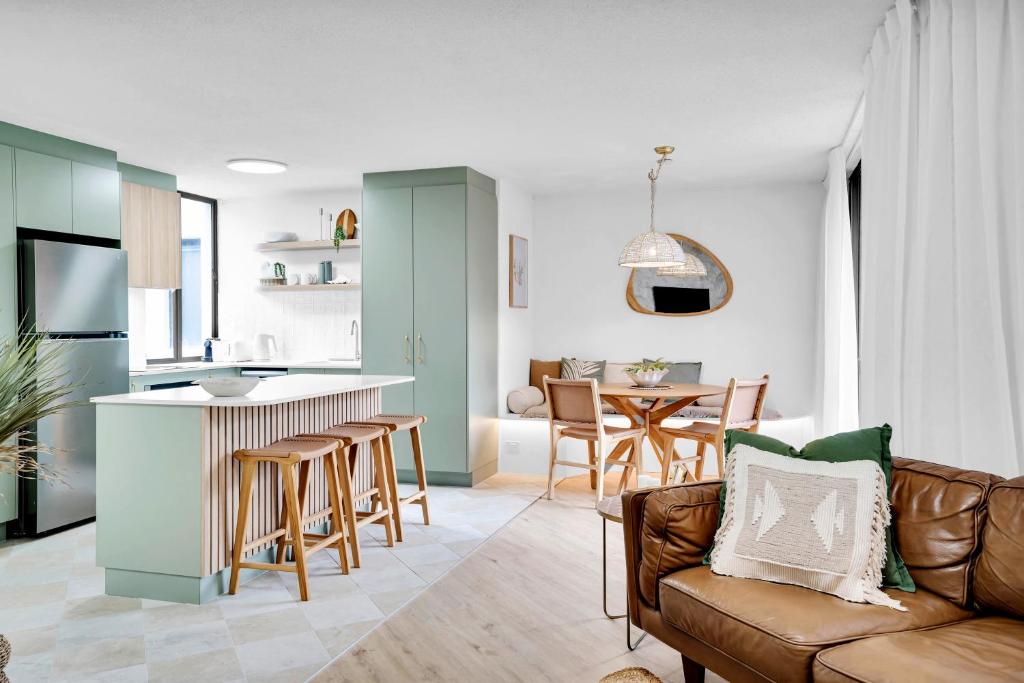 a living room with a couch and a kitchen at Beachfront Beauty in Alexandra Headland