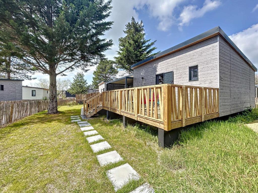 un mobile home avec une terrasse en bois dans une cour dans l'établissement Chalet cosy avec piscine chauffée, terrasse et parking à 2 pas de la plage de Jullouville - FR-1-361-480, à Jullouville