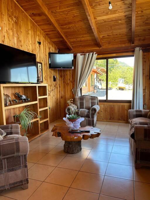 ein Wohnzimmer mit einem TV, Stühlen und einem Tisch in der Unterkunft Cabaña Flor de Lican in Licán Ray
