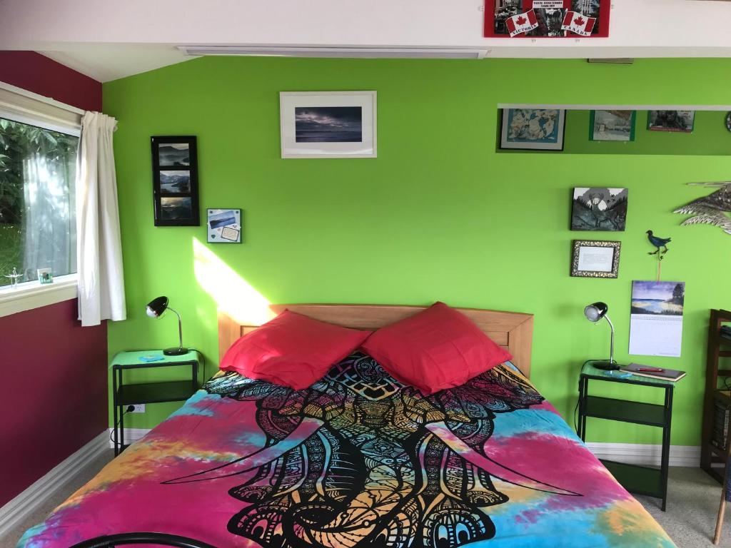 Schlafzimmer mit grünen Wänden und einem Bett mit roten Kissen in der Unterkunft Piringa in Dunedin