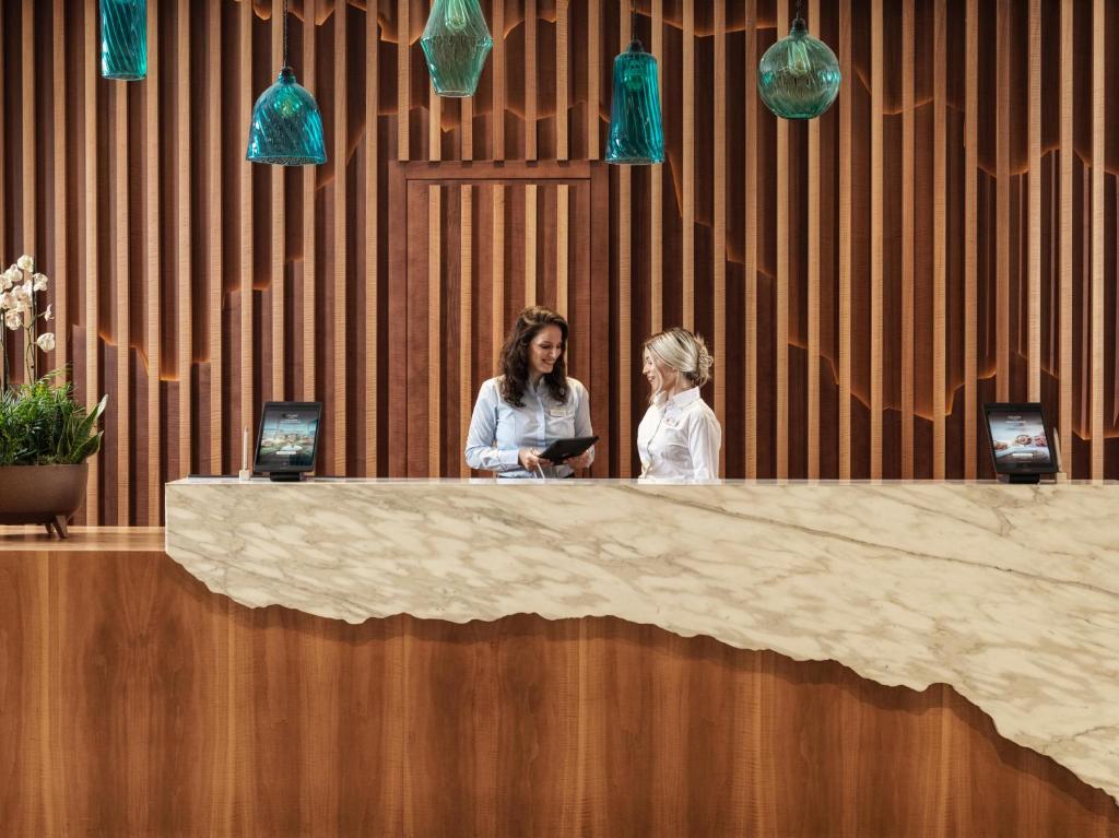 two women standing at a reception desk with their phones at The Chedi Luštica Bay in Tivat