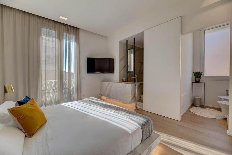 a white bedroom with a large bed and a bathroom at Le Palmette Suites in Cagliari