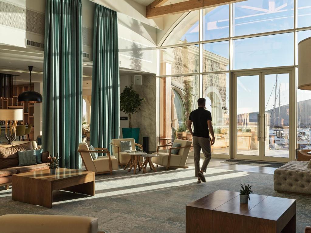 a man walks through a living room with large windows at The Chedi Luštica Bay in Tivat