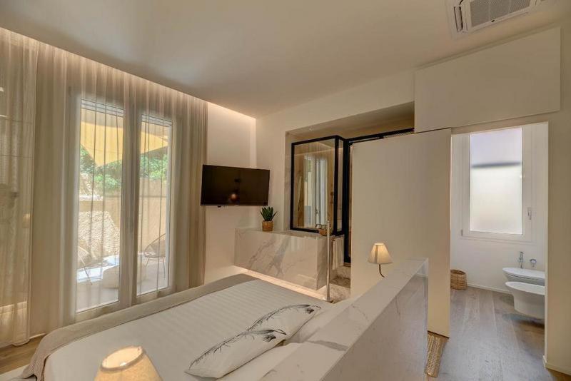 a white bedroom with a large bed and a bathroom at Le Palmette Suites in Cagliari