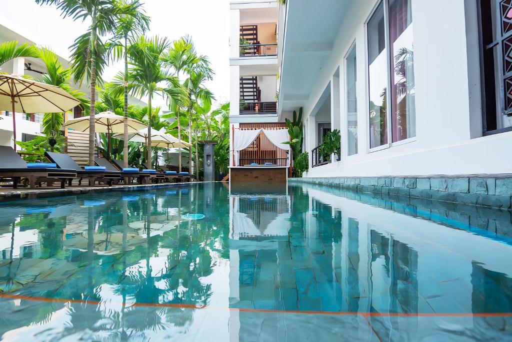 a swimming pool next to a building with palm trees at SAKABAN Suite in Siem Reap