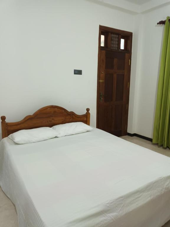 a bed with white sheets and a wooden headboard in a room at White's vila in Matara