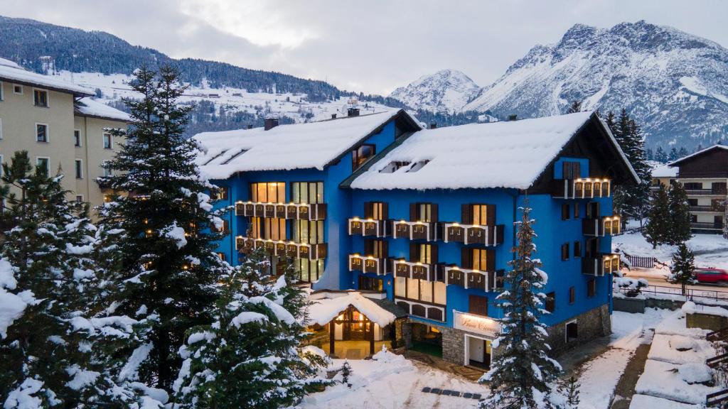 un edificio blu con montagne innevate sullo sfondo di Hotel Baita Clementi a Bormio